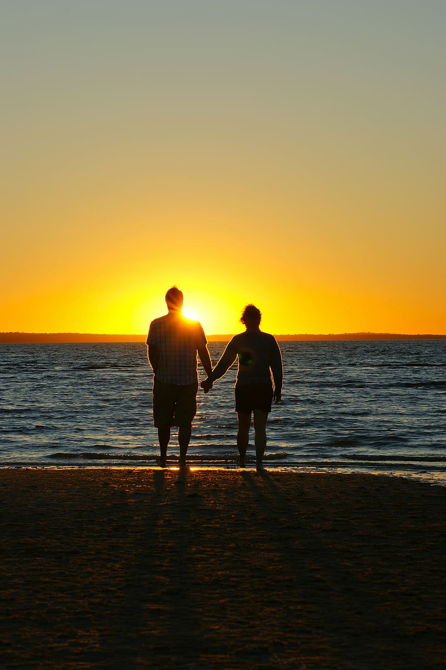 A couple holding hands on a beach with a sunset in the background.