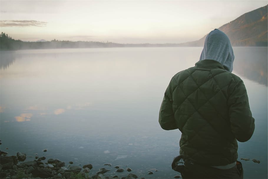 A person standing by a body of water, contemplating and looking into the distance.