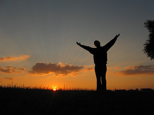 A person standing in a field with their arms outstretched, looking towards the sky.