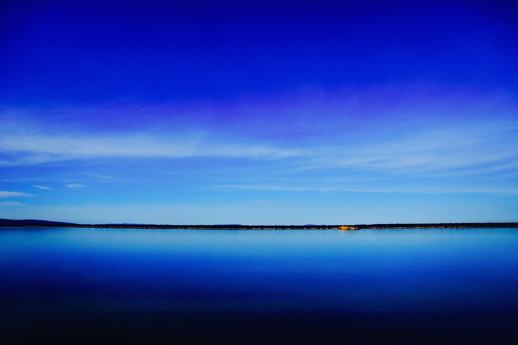Clear blue sky reflecting on calm ocean water